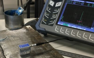 Ultrasonic testing on a welded metal piece with measurement device and display.
