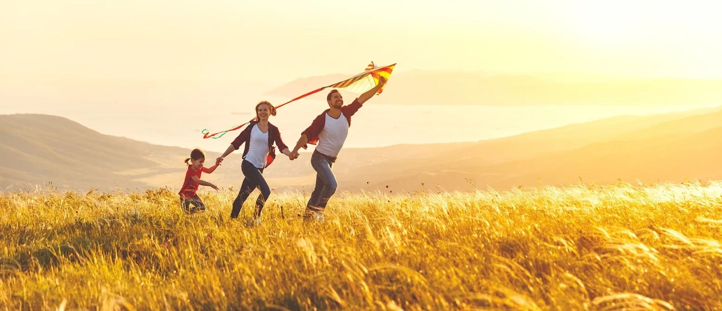 Young girl, mother, and father running with a kite in a field at sunset