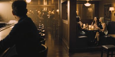 Three women talking in a cozy bar booth while a man sits at the bar.