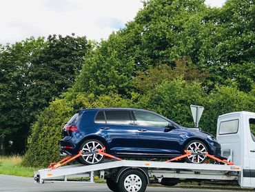 Blue car secured on a white flatbed tow truck.