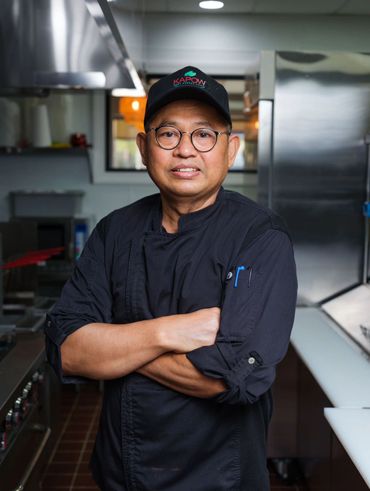 Chef in a black uniform and cap standing confidently in a kitchen.