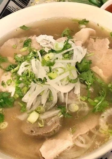 A bowl of Vietnamese pho with beef, onions, and herbs in clear broth.