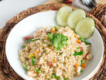 A bowl of vegetable fried rice garnished with cilantro and cucumber slices.