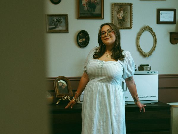 Woman in a white dress posing indoors with framed artwork behind her.