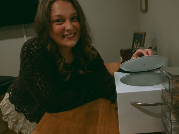 A woman smiling while opening a small appliance on a wooden table.