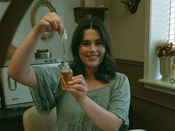 Woman smiling while holding a dropper bottle of skincare product.