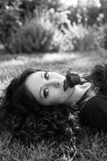Woman lying on grass holding a rose in her mouth, black and white photo.