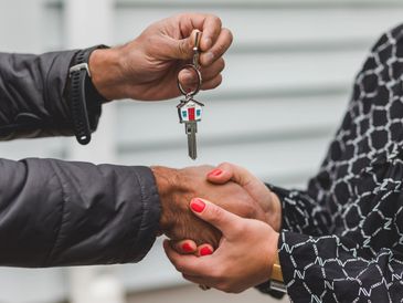 Two people shaking hands with a house key keychain symbolizing homeownership.