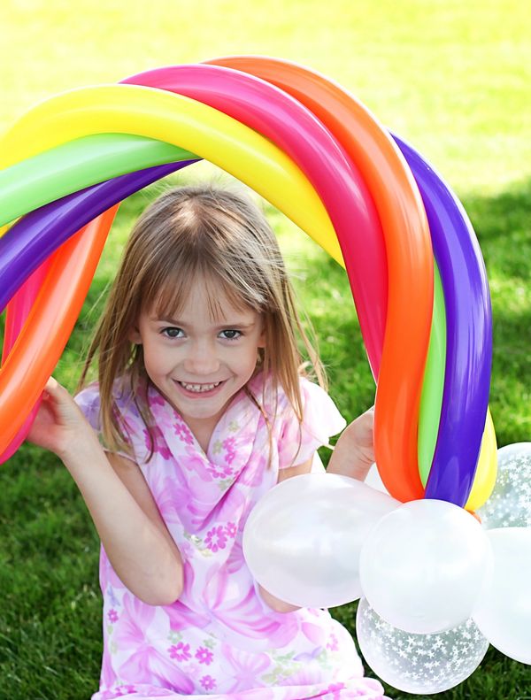Birthday Girl holding a balloon twisted rainbow with clouds.