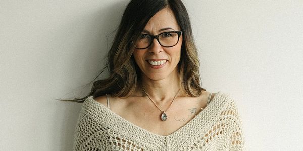 Smiling woman with glasses wearing a knitted shawl.