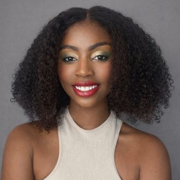 Smiling woman with curly hair and vibrant makeup in a beige sleeveless top.