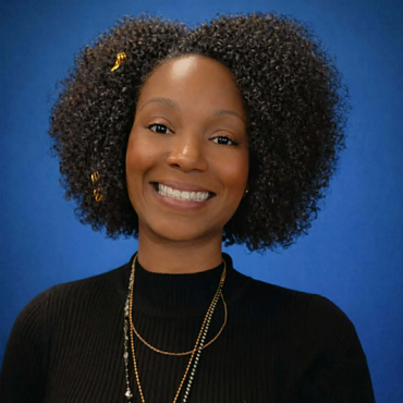 Smiling woman with curly hair and layered necklaces against blue background.