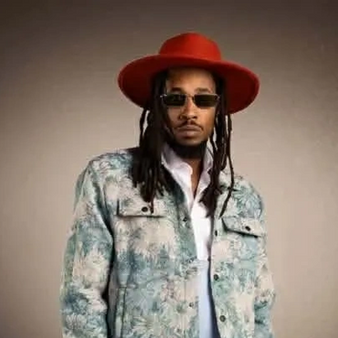 Man in a red hat, patterned jacket, white pants, and sunglasses posing confidently.