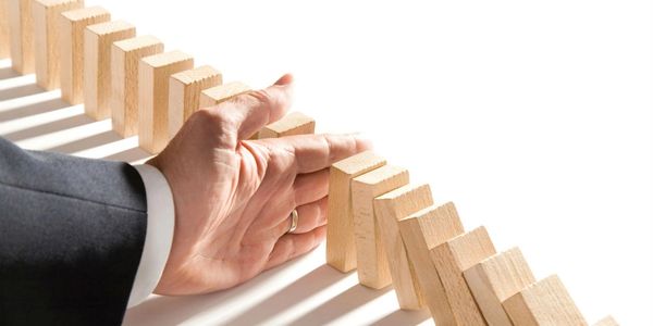 Left hand of a business man extended to stop row of wooden blocks from falling like dominos.