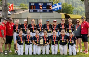 Softball team celebrating championship win with medals and trophy.