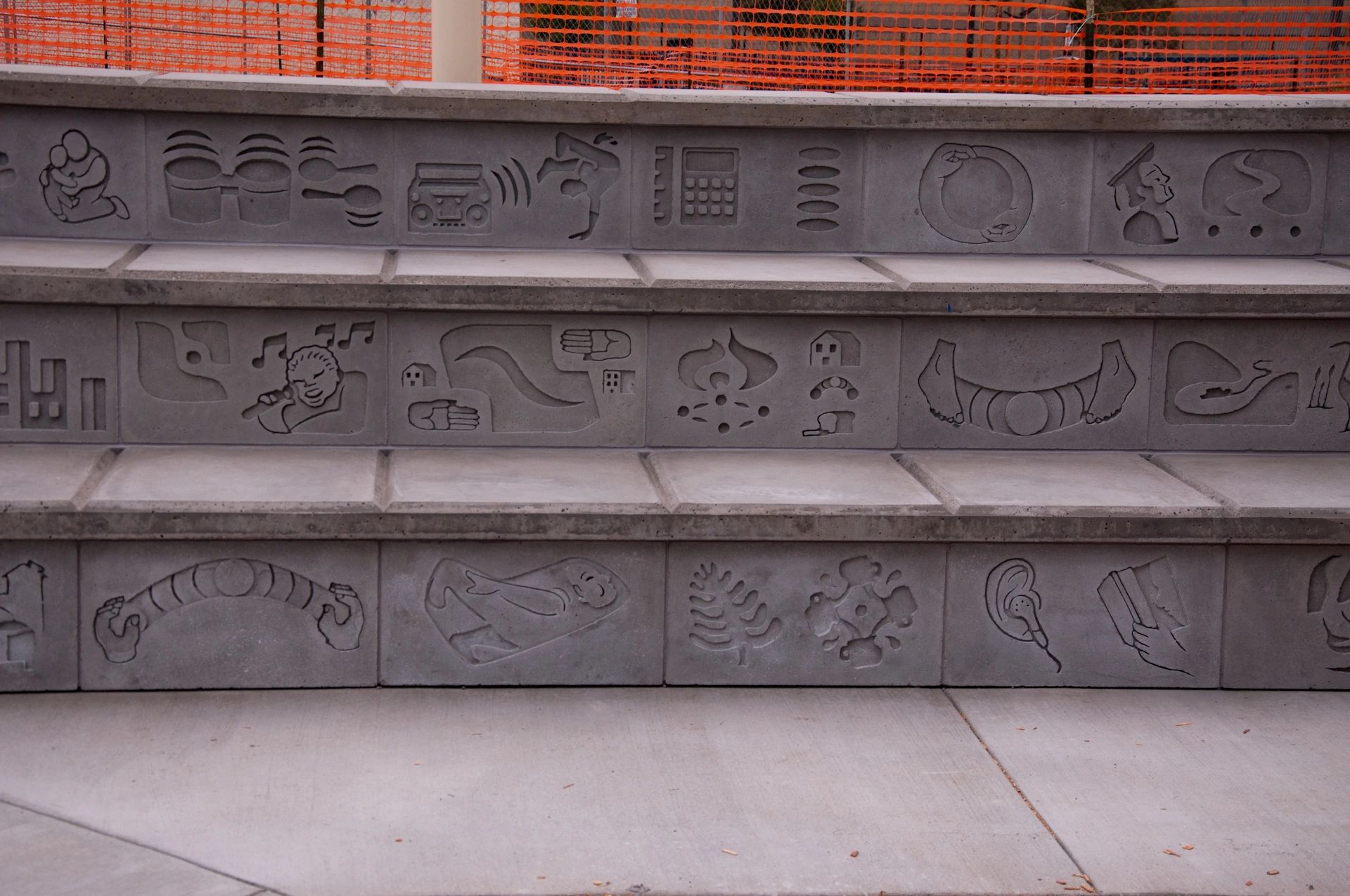 Three rows of decorative concrete bas relief tiles on amphitheater seating viewed up close.