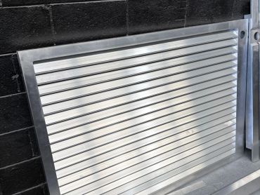Metal vent panel leaning against a black brick wall.