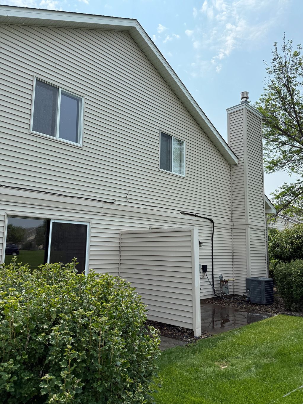 Side view of a beige vinyl-sided house with windows and greenery.