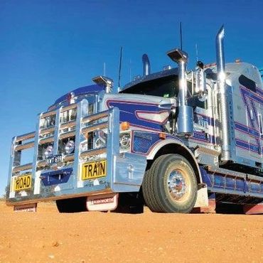 A large, shiny road train truck on a sandy ground under a clear blue sky.