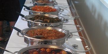 A buffet table with multiple stainless steel chafing dishes filled with various cooked dishes.