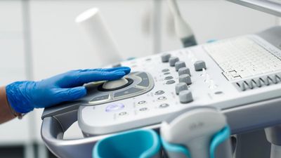 Hand in blue glove operating ultrasound machine controls.