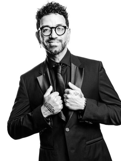 Man in glasses and suit adjusting his jacket, smiling confidently.