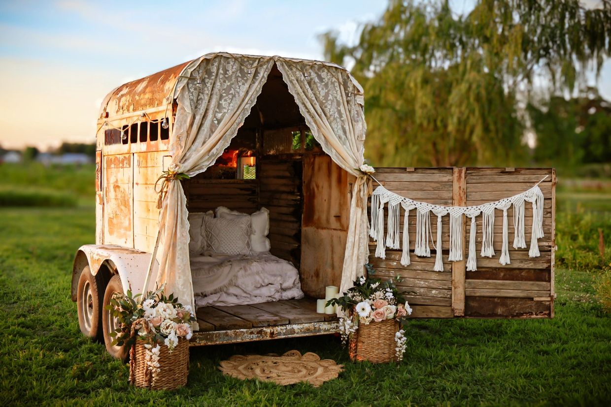Rustic trailer converted into a cozy outdoor nook with lace curtains and floral decor.
