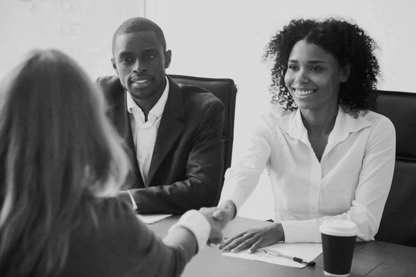 a woman shaking another woman's hand at the desk with a man sitting next to them