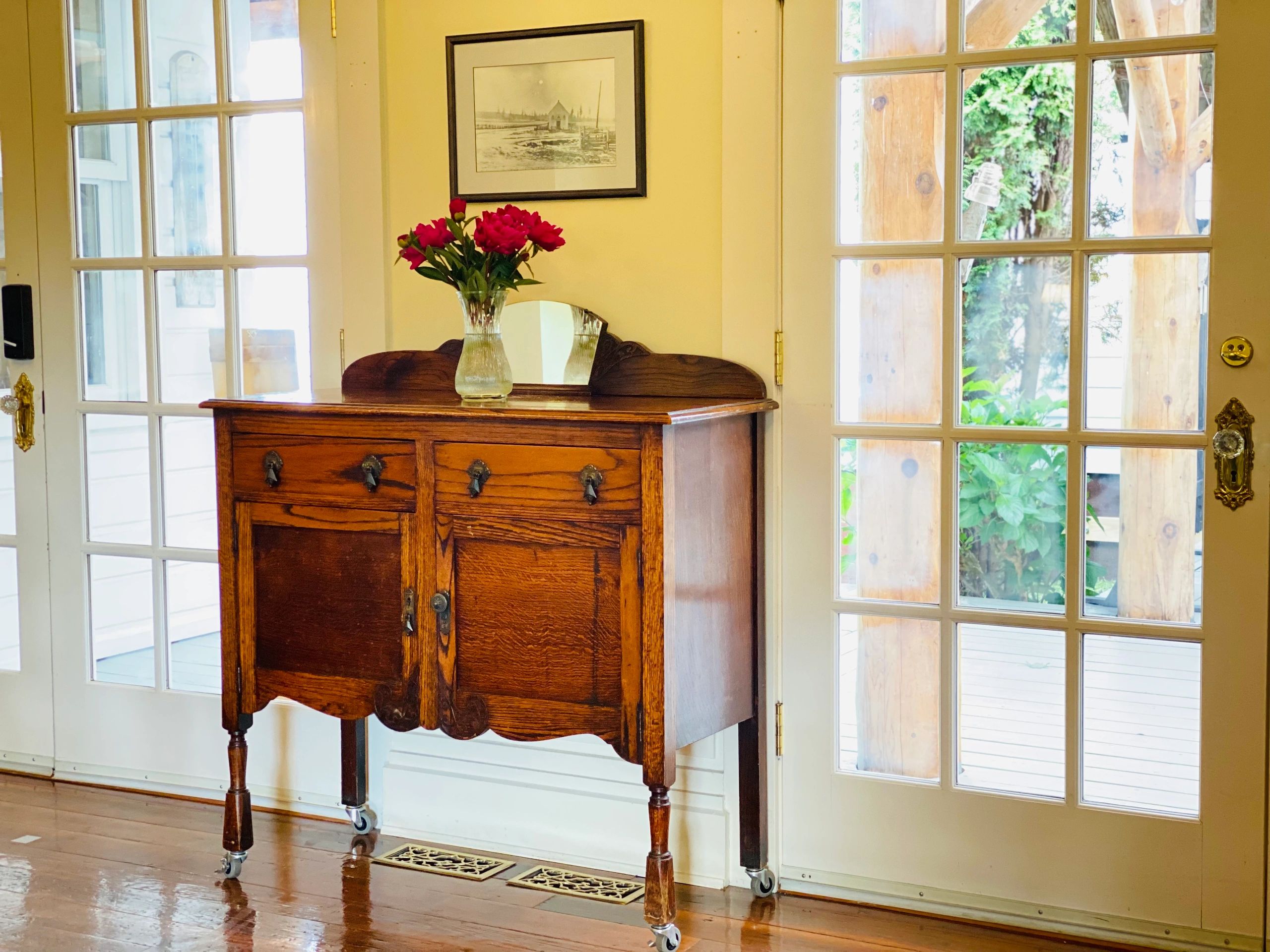 Antique sideboard cabinet with vase of fresh flowers between french doors at Princess and the Pea Ho