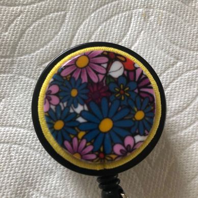 ID Badge reel has multiple colored flower design with yellow cording on black badge reel