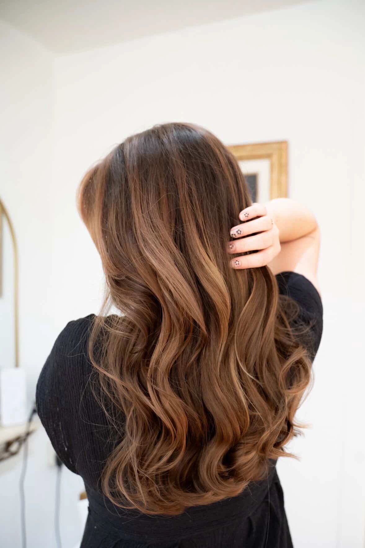 Soft caramel balayage on long wavy brown hair, back view, at The Parisian Hair Salon in Largo, FL