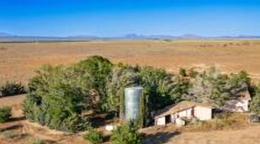 Isolated farmhouse surrounded by trees in a vast desert landscape.