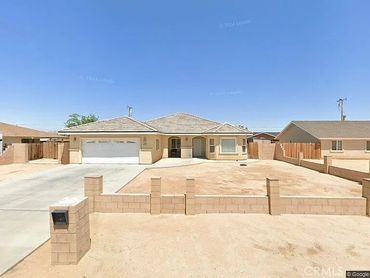Single-story house with a large driveway and desert landscaping under a clear blue sky.