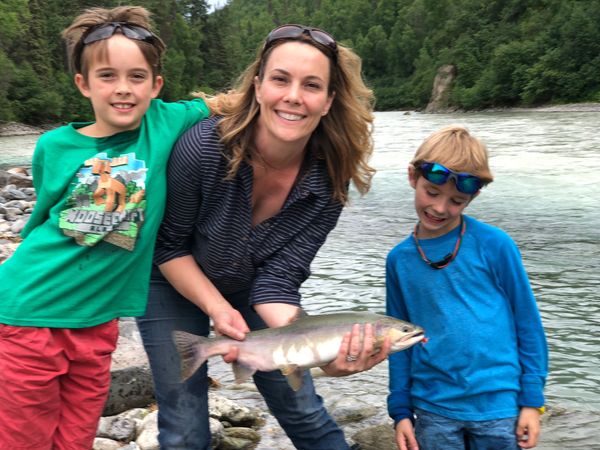 A woman and two boys proudly showing a large fish by a river.