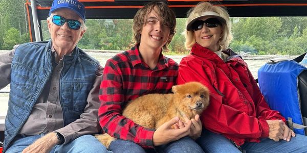 Three people and a dog sitting together outdoors, smiling and enjoying a trip.