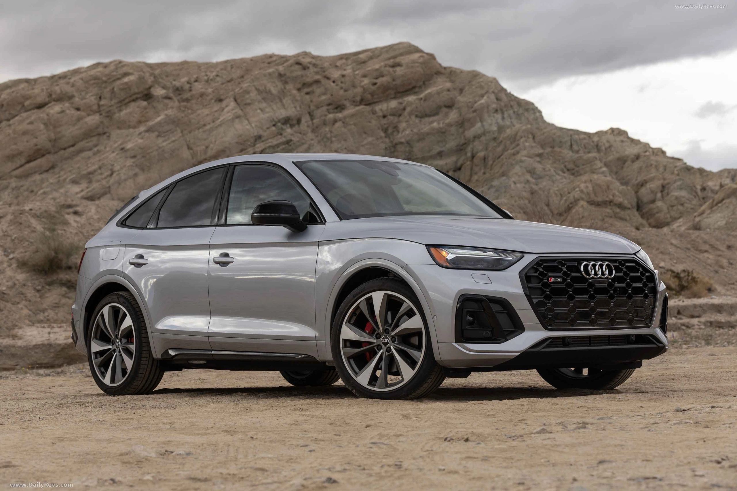 Silver Audi Q5 SUV parked on a sandy terrain with rocky hills in the background.
