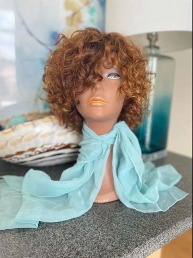 Mannequin head with curly hair and blue scarf on table.