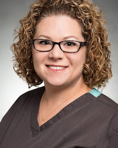 Image of a smiling woman with curly hair and glasses in medical scrubs.