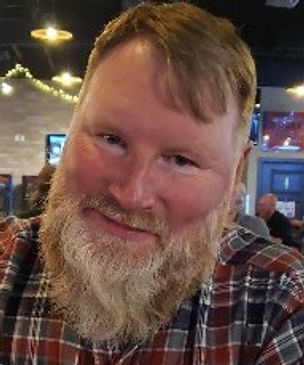 Smiling man with a beard in a cozy indoor setting.