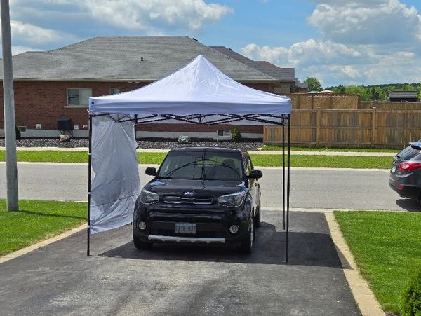 Black car parked under a white canopy tent in a driveway.