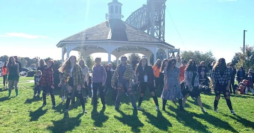 A group of young people dressed in torn clothes posing outdoors near a gazebo.