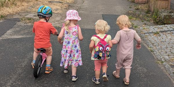 Die Kinder gehen Hand in Hand den Fußweg entlang.
