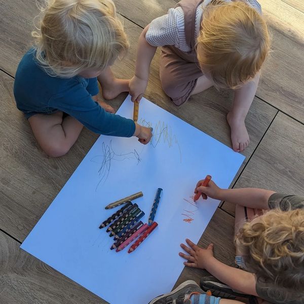 Die Kinder malen mit Stiften auf einem großen Blatt auf dem Boden.