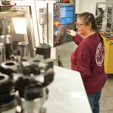Student operating Computer Integrated Machining equipment with blurred cutting heads in foreground