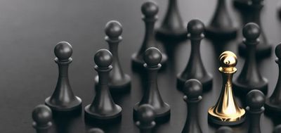 A golden pawn stands out among many black pawns on a dark surface.