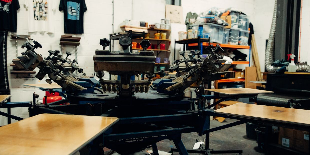 Screen printing machine in a workshop with shelves and supplies.