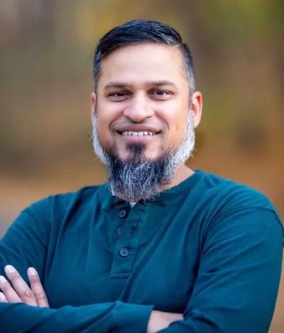 Smiling man with a beard in a blue shirt, arms crossed.