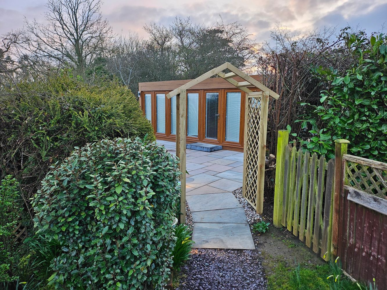 Garden path leading to a wooden structure with glass doors at sunset.