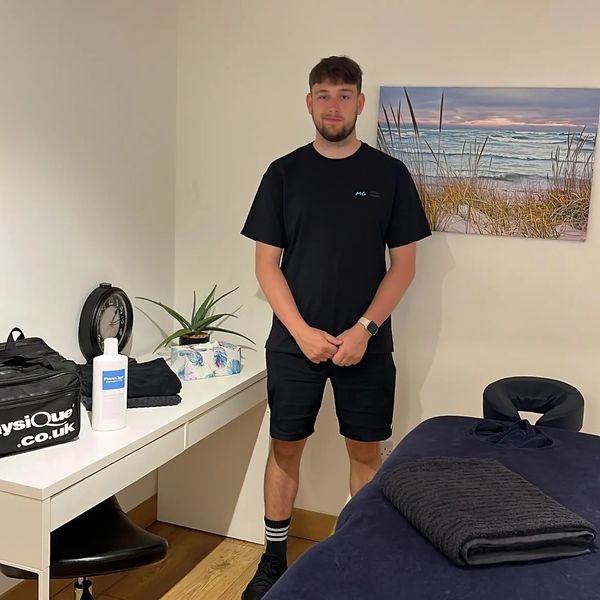 A man stands in a tidy room with massage equipment and decor.