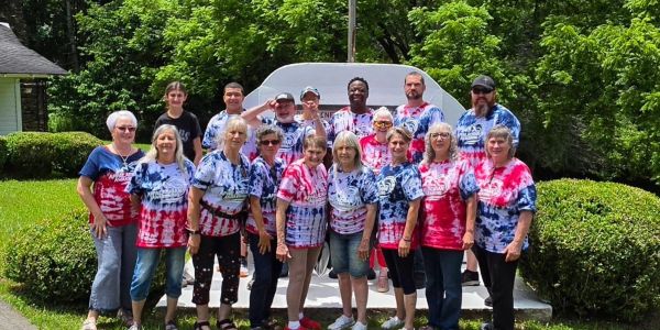 Group photo of people in colorful tie-dye shirts outdoors.